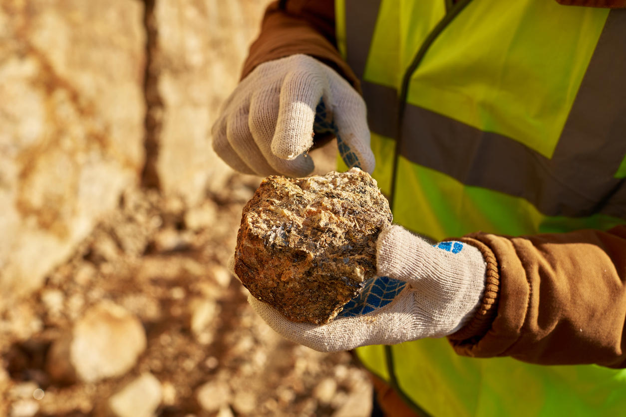 Worker in high vis and gloves holding rock with gold at a mine site