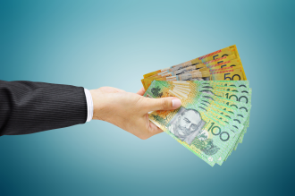 A hand belonging to a man in a suit hands over hundreds of dollars of Australian cash to an unseen recipient 