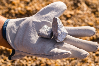 A gloved hand in an outback setting reminiscent of a geologist holds some kind of illustrious rock 