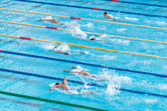 Competitors race one another in a butterfly style swimming race in an olympic length swimming pool. Swimming is one of the largest events of each Olympic games