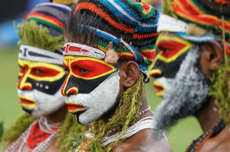 Three performers adorning traditional tribal paints perform at a ceremony in PNG at an unknown location and date