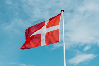 The red flag of the Kingdom of Denmark flies beneath a blue sky