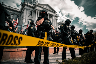 Militarised police guard a government building in Denver, US, while protesters holding Trump signage are featured in the background