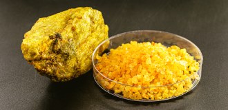 A hard-rock sample of uranium ore next to a nitrate product in a glass dish 