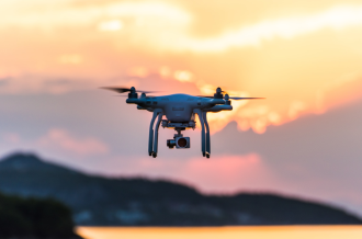 A drone available on the retail market flies in the foreground with a sunset background out of focus
