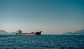 A tanker ship sits in the midground of the ocean with mountains in the distance suggesting a bay 