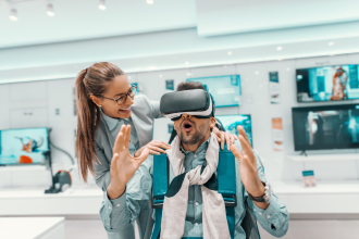 VR - Amazed mixed race man sitting in chair and trying out vr technology. Woman standing next to him and holding his shoulders. Tech store interior