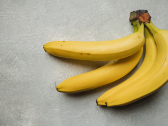 A bunch of three bananas are photographed on a grey table