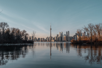 A small estuary-like inlet is featured in the foreground, in the background, the city skyline of Ontario is featured in the morning light
