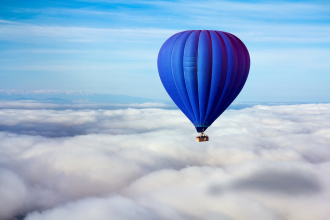 A blue hot air balloon flies above cloud cover 