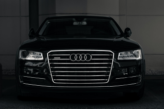 A sleek black Audi sedan faces the camera head on in an atmospherically lit dark carpark