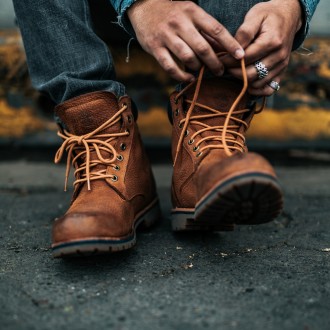A man ties the shoelaces on a pair of brown boots designed for rough terrain 