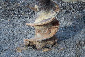 An auger drill bit pictured sinking into gravel-like rock 