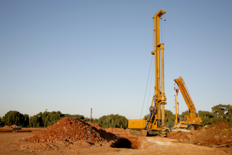 A photograph of a drill rig stained with Pindan dirt underneath a blue sky pictured in an outback setting