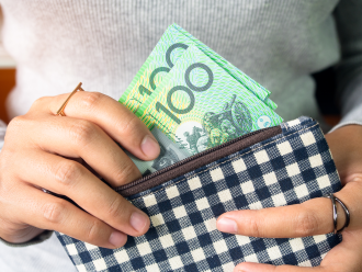 An individual retrieves a selection of Australian one hundred dollar notes from a checkered wallet 