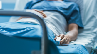 An anonymous patient rests in a hospital bed in blue dressing with a heartrate monitor atteched to their finger 