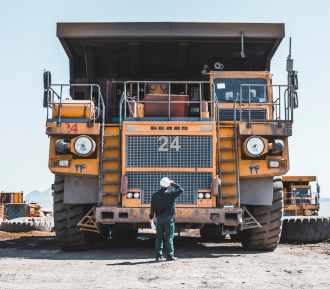 person wearing hard hat standing in front of big yellow mining truck