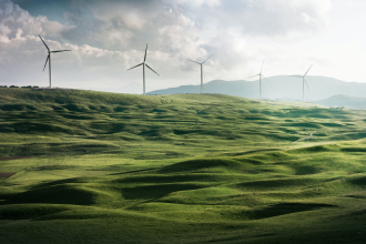 A row of wind turbines stand in the midground of a green valley 