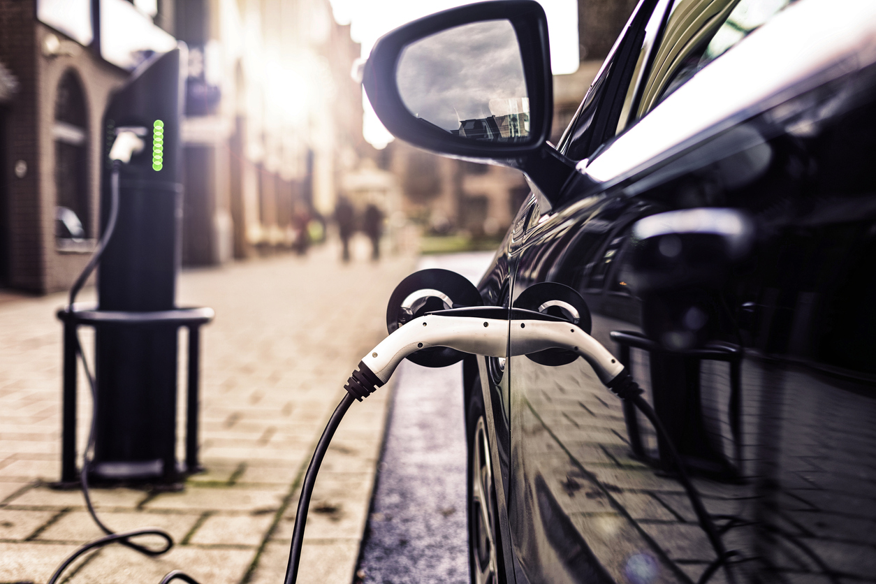 A black EV plugged into a public roadside charging station