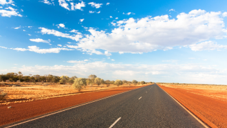 A road stretching to the horizon in the Australian outback beneath a blue sky 