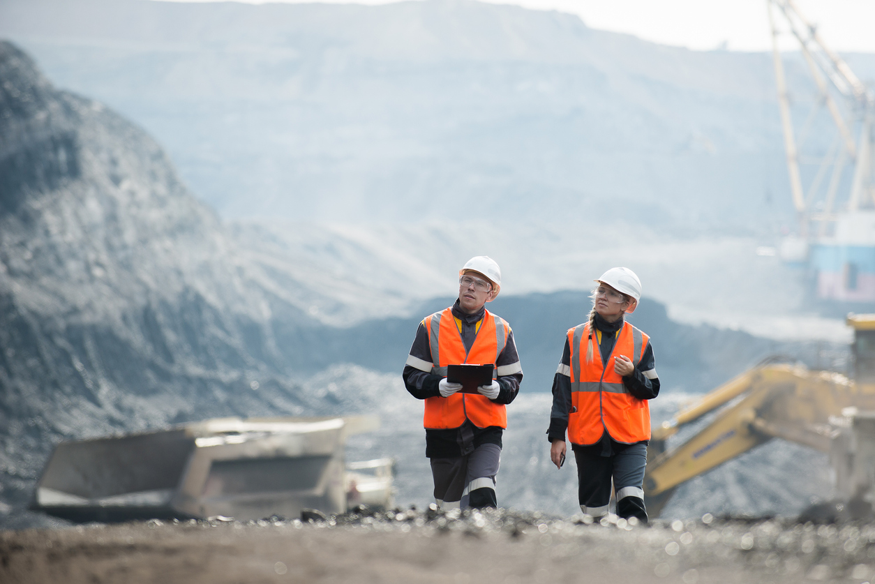Mining - Two workers in hard hats and high vis walking through a mine site