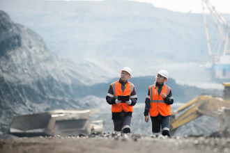 Mining - Two workers in hard hats and high vis walking through a mine site
