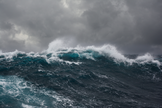 A king wave gathers momentum in a stormy ocean beneath a grey cloudy sky 
