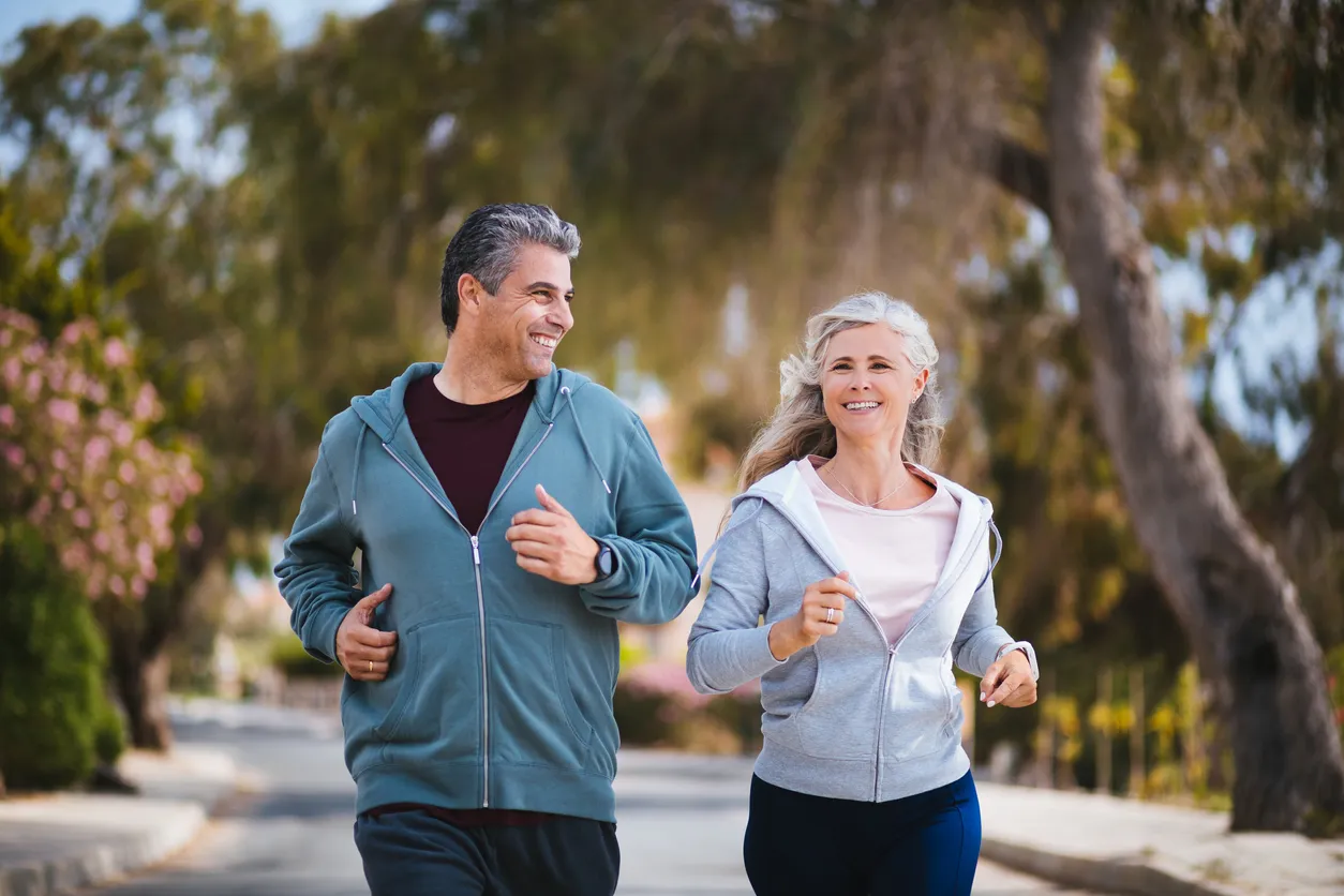 Happy man and woman jogging and smiling down treelined street