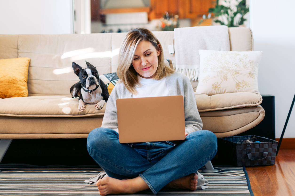 Young woman using laptop with terrier in sunny room.
