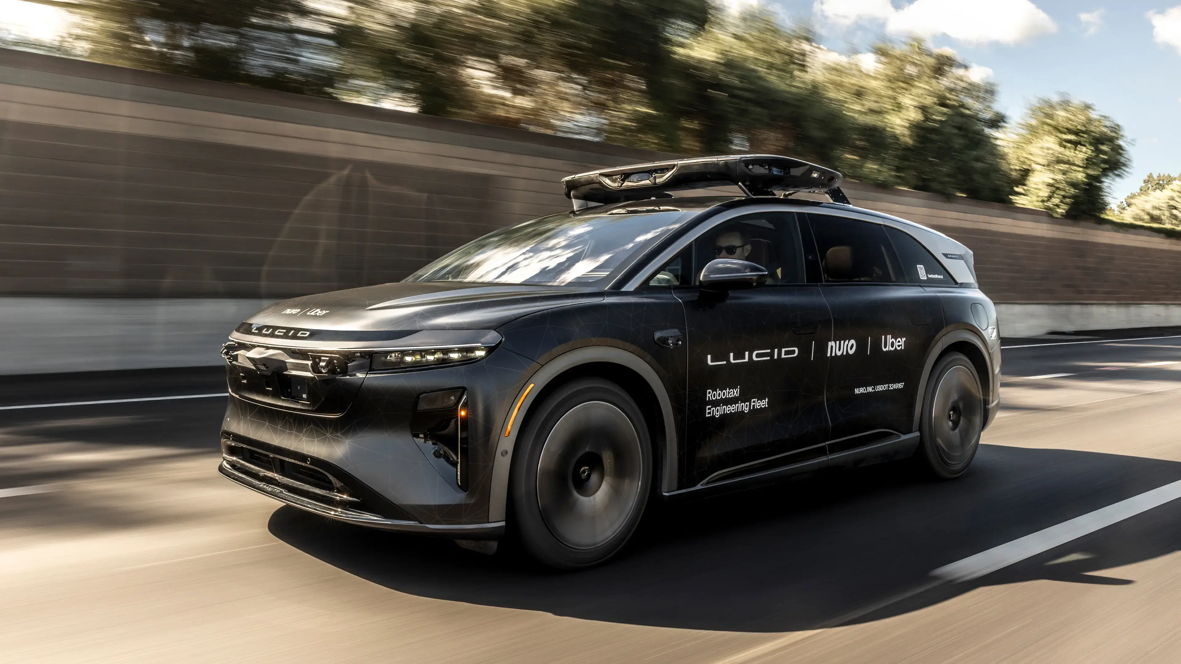 Black Lucid autonomous vehicle with roof sensors driving on highway, branded as "Robotaxi Engineering Fleet" for Uber and Nuro.