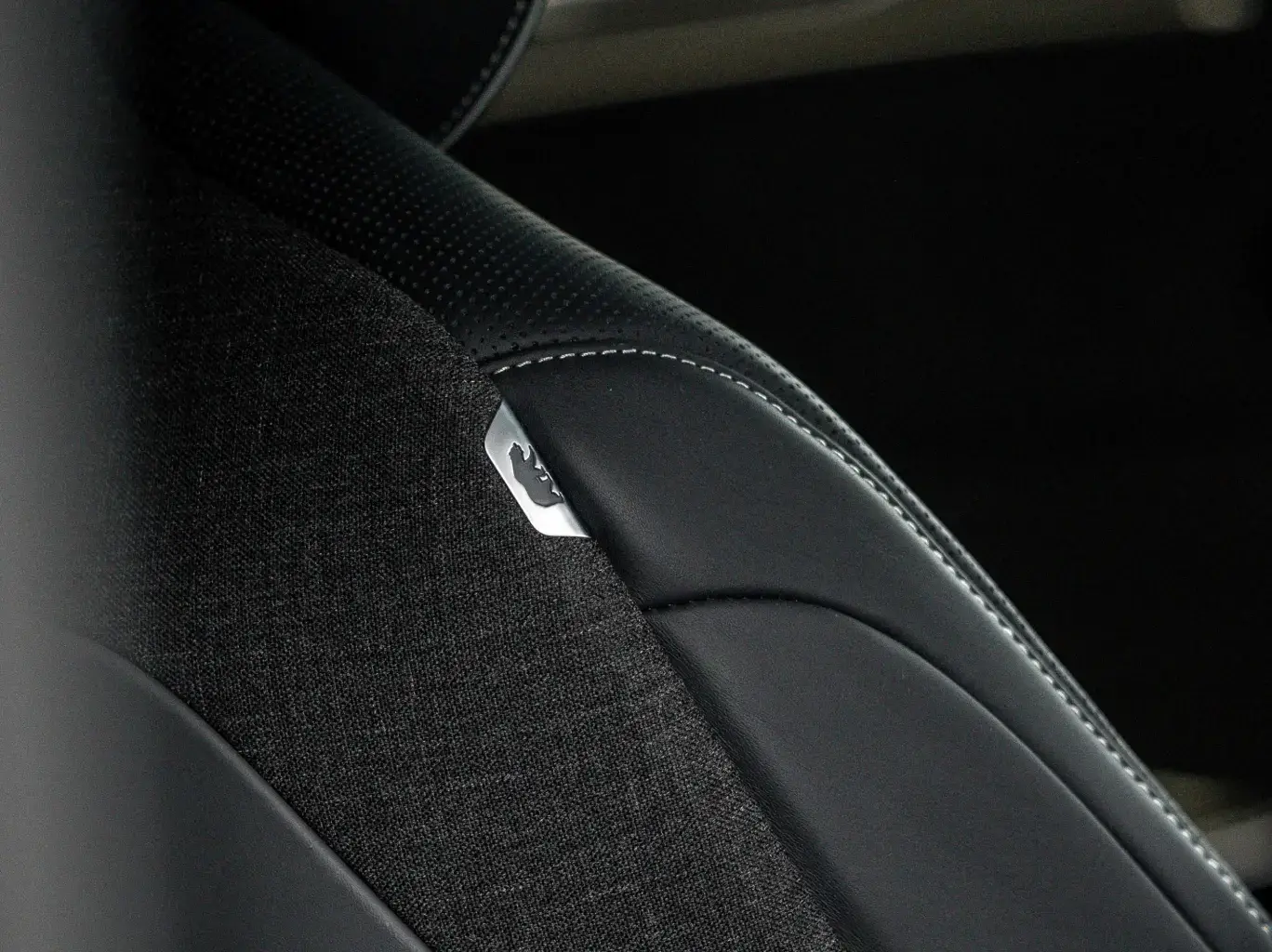 Close-up of a car seat with black leather trim and fabric upholstery, showing contrast stitching and a small bear logo.