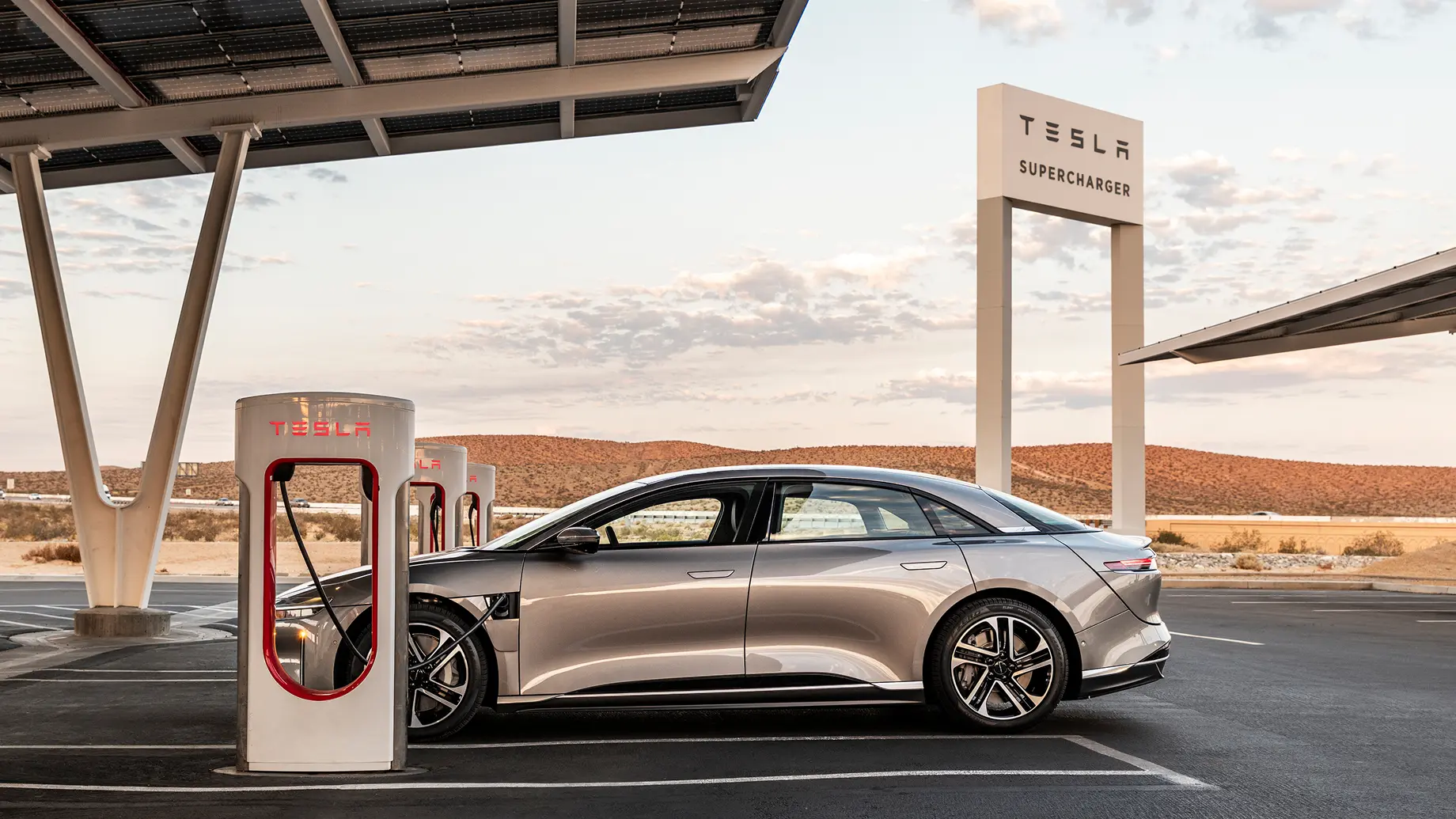 Lucid Air vehicle charging at a Tesla Supercharger station with desert landscape in the background.