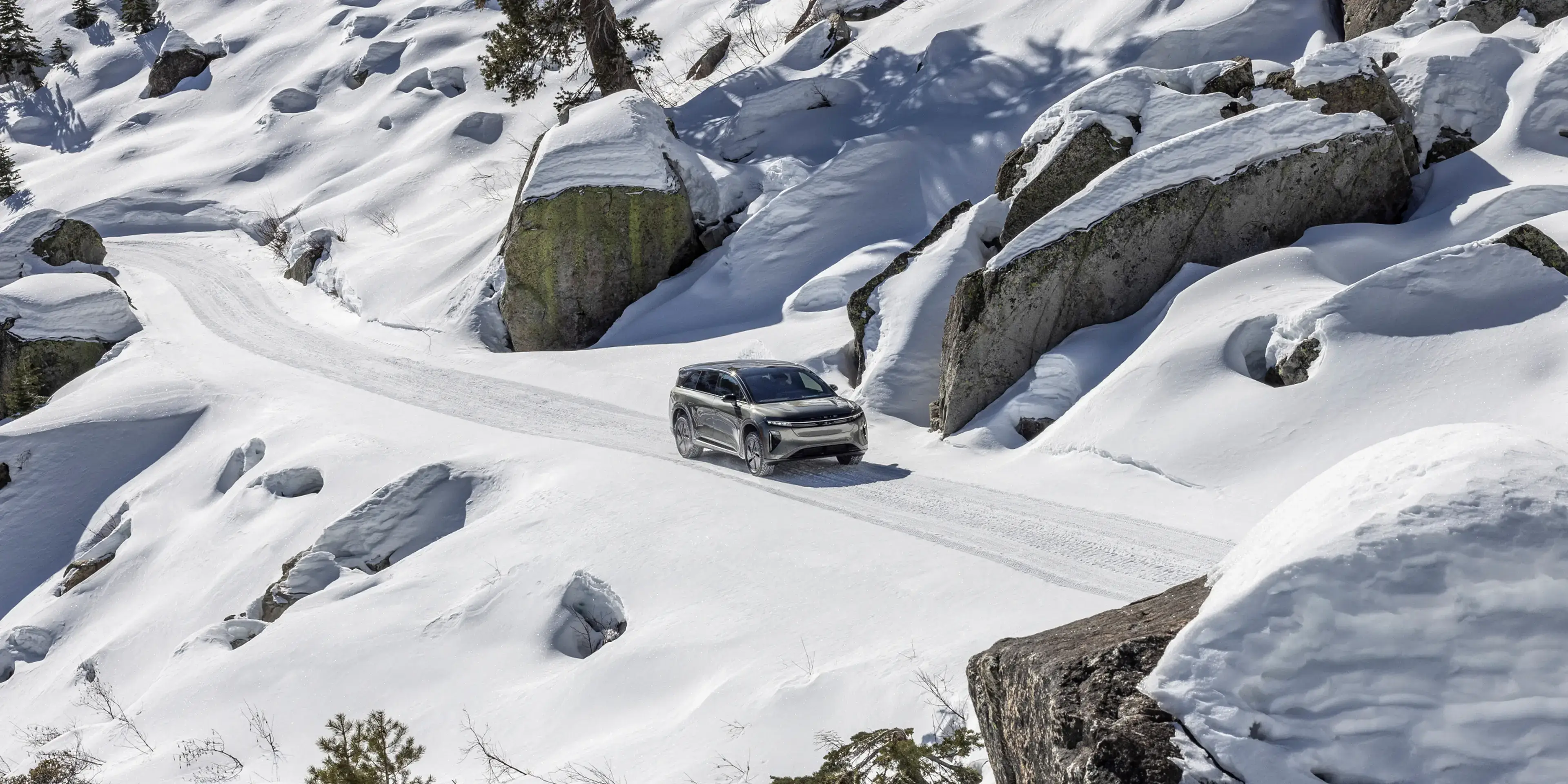 Un Lucid Gravity circulant sur une route de montagne enneigée, entourée de gros rochers enneigés dans un paysage rocailleux.