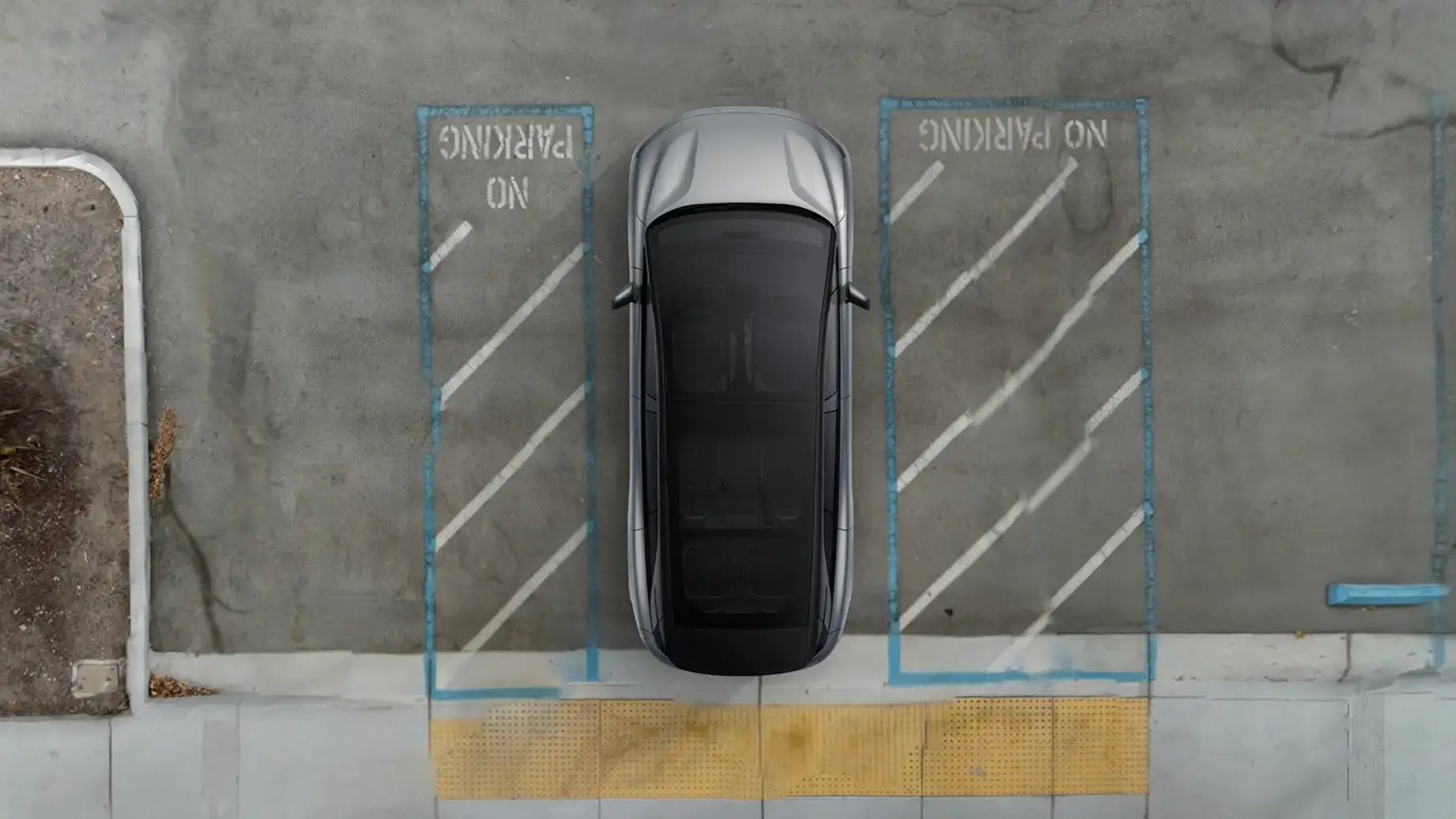 Aerial view of a silver car parked between two blue-outlined "No Parking" zones on a concrete surface.