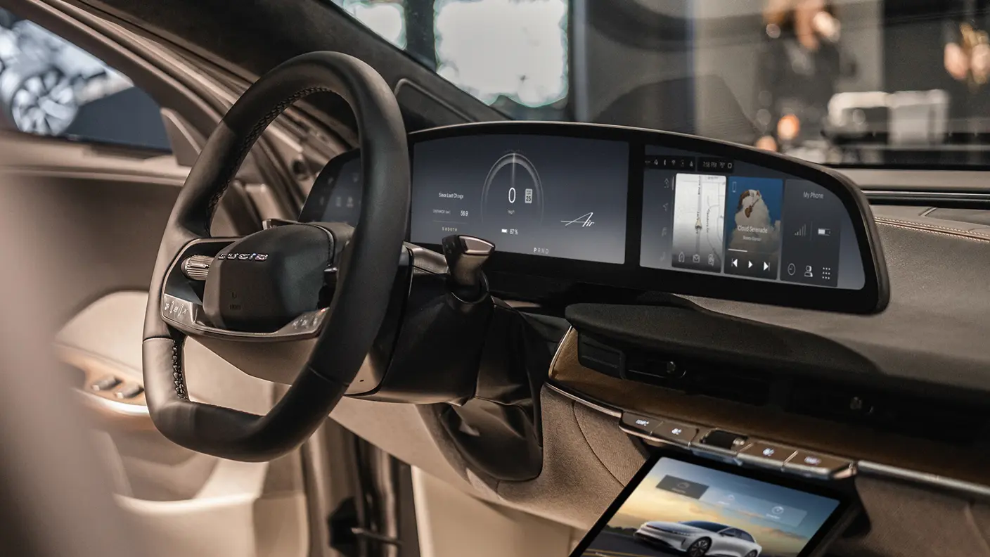 Lucid Air luxury EV interior featuring a black steering wheel, wide curved digital dashboard, and center touchscreen display.
