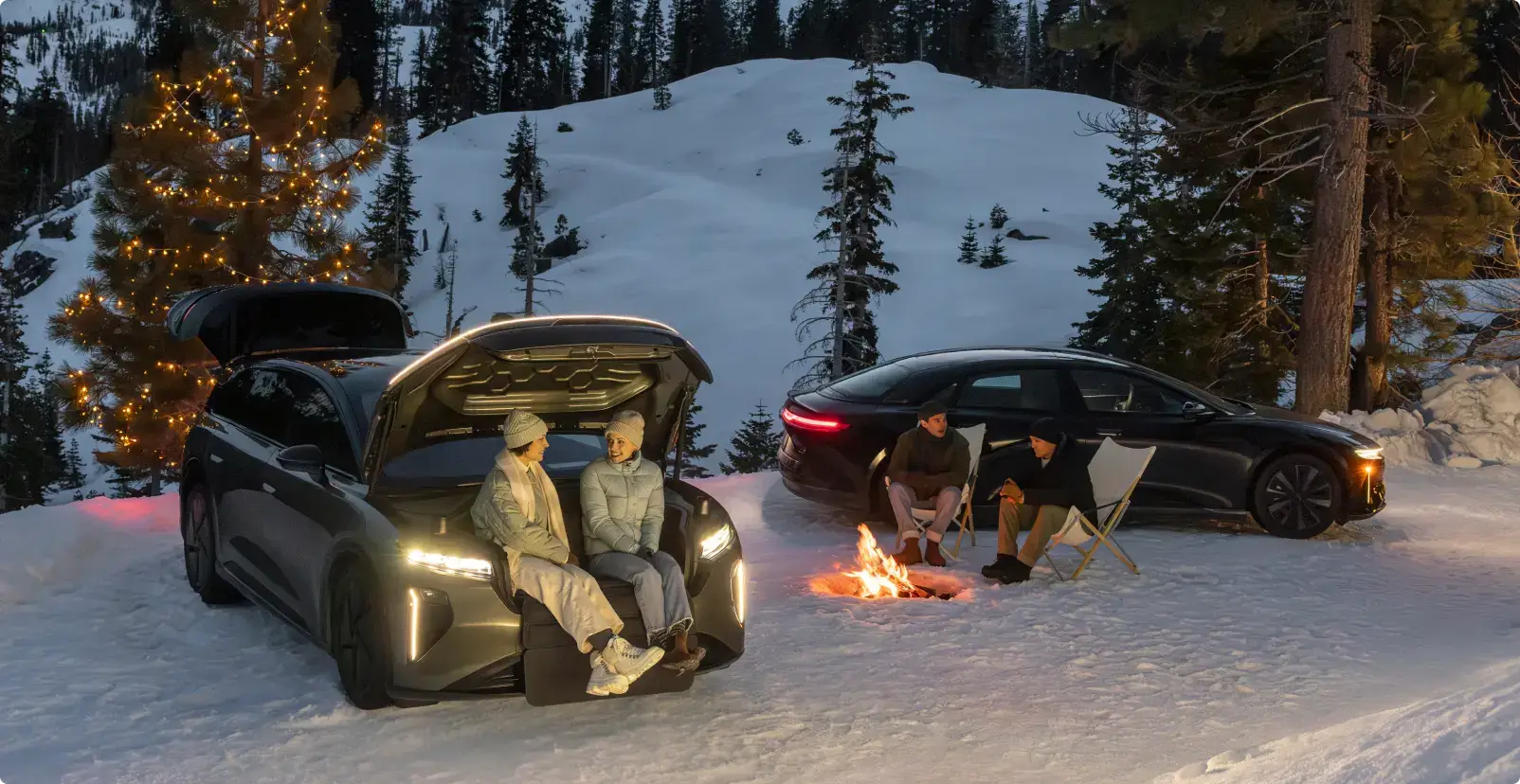 People enjoying winter camping with Lucid vehicles, sitting by a campfire in snowy mountains with a lit Christmas tree nearby.