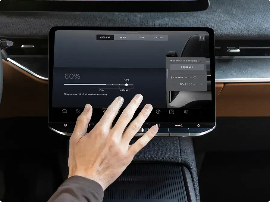 Hand touching car dashboard touchscreen showing EV charging interface at 60% with scheduled charging options.