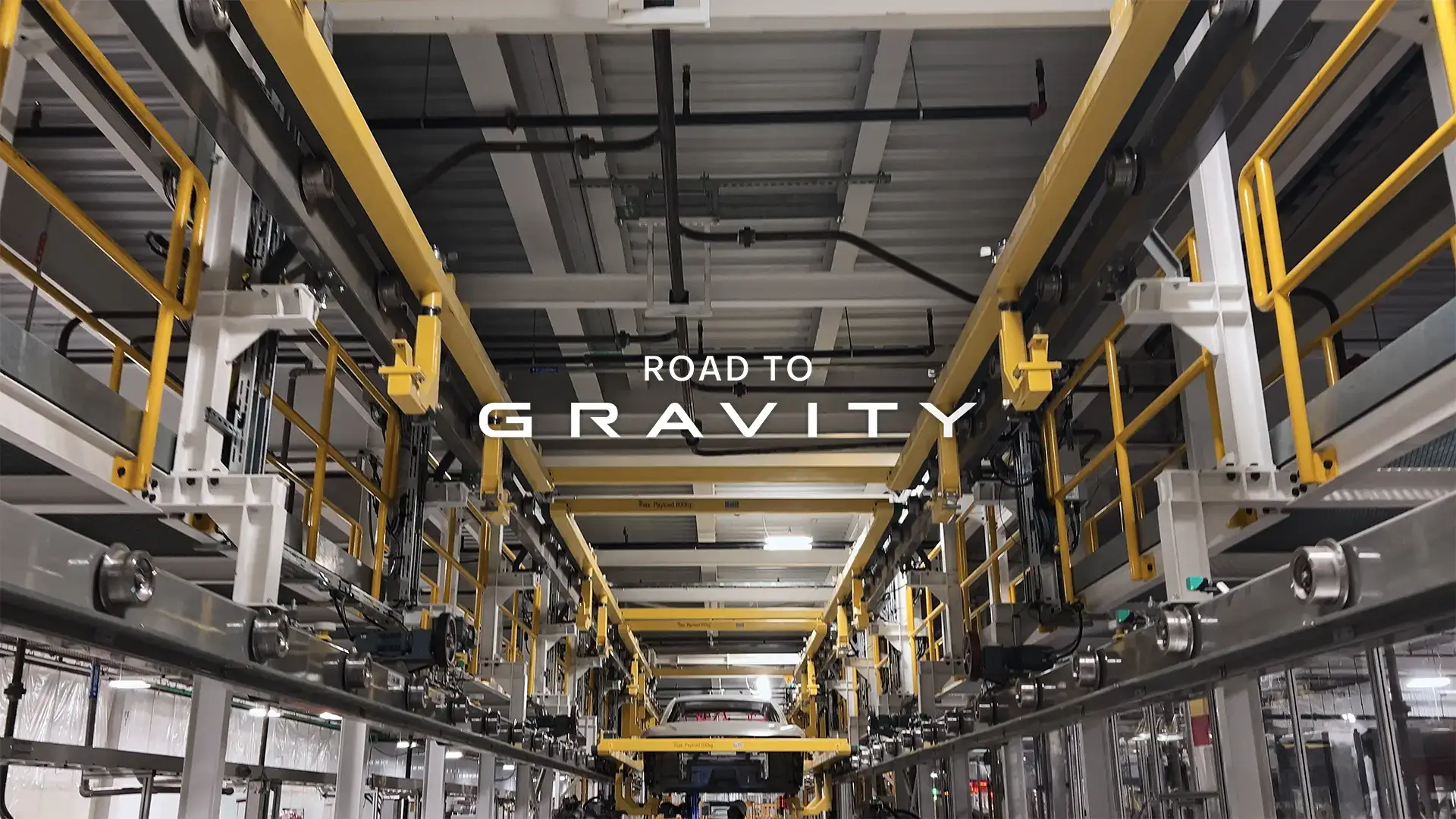 Industrial automotive assembly line with yellow safety rails and "ROAD TO GRAVITY" text overlaid in white letters.