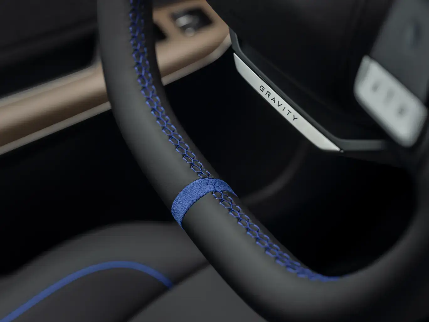 Close-up of a black steering wheel with blue stitching and a "Gravity" badge, set against a dark interior.