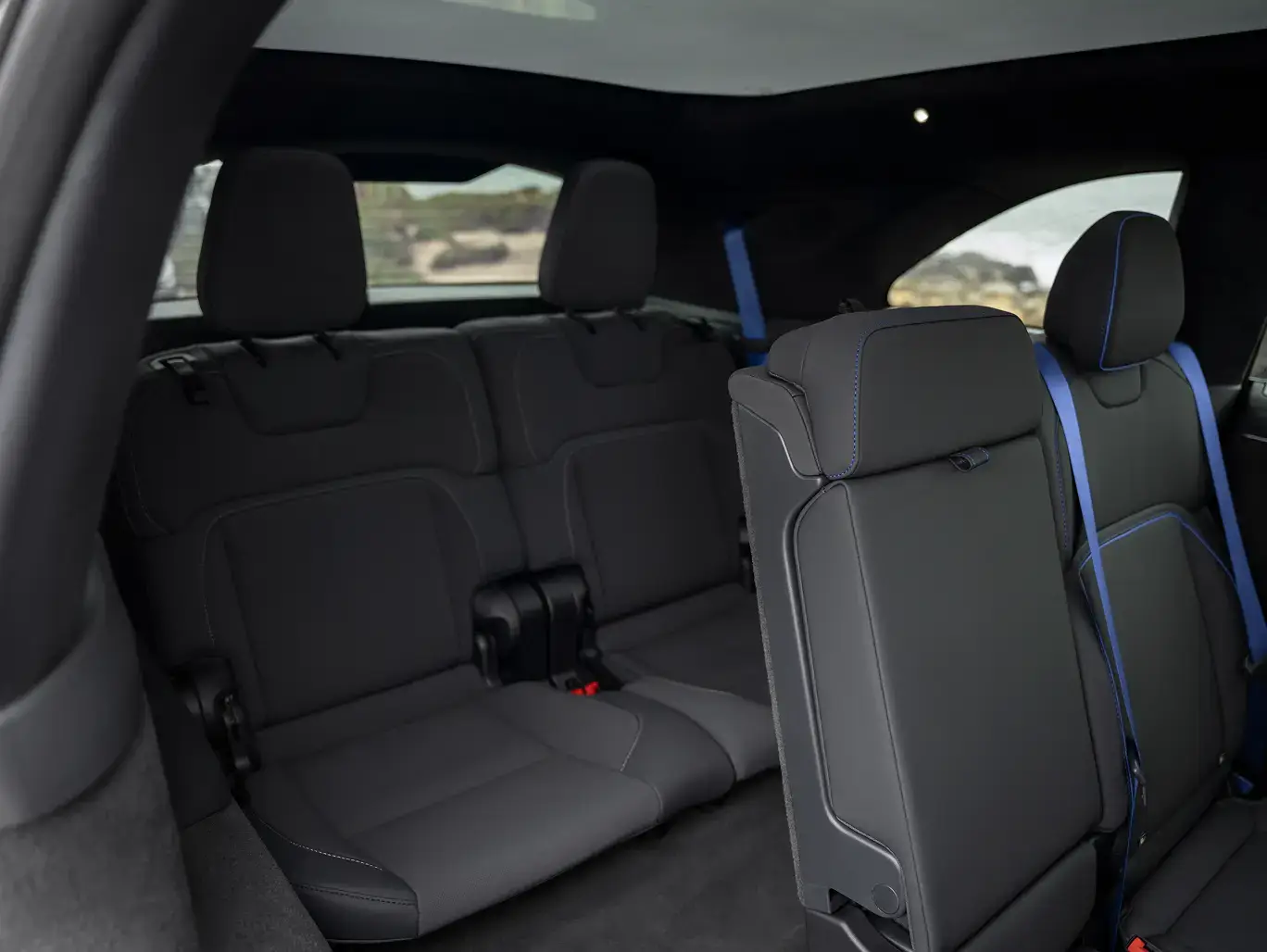 SUV interior showing dark gray rear seats with blue accent stitching and seatbelts, panoramic roof, and scenic view through windows.