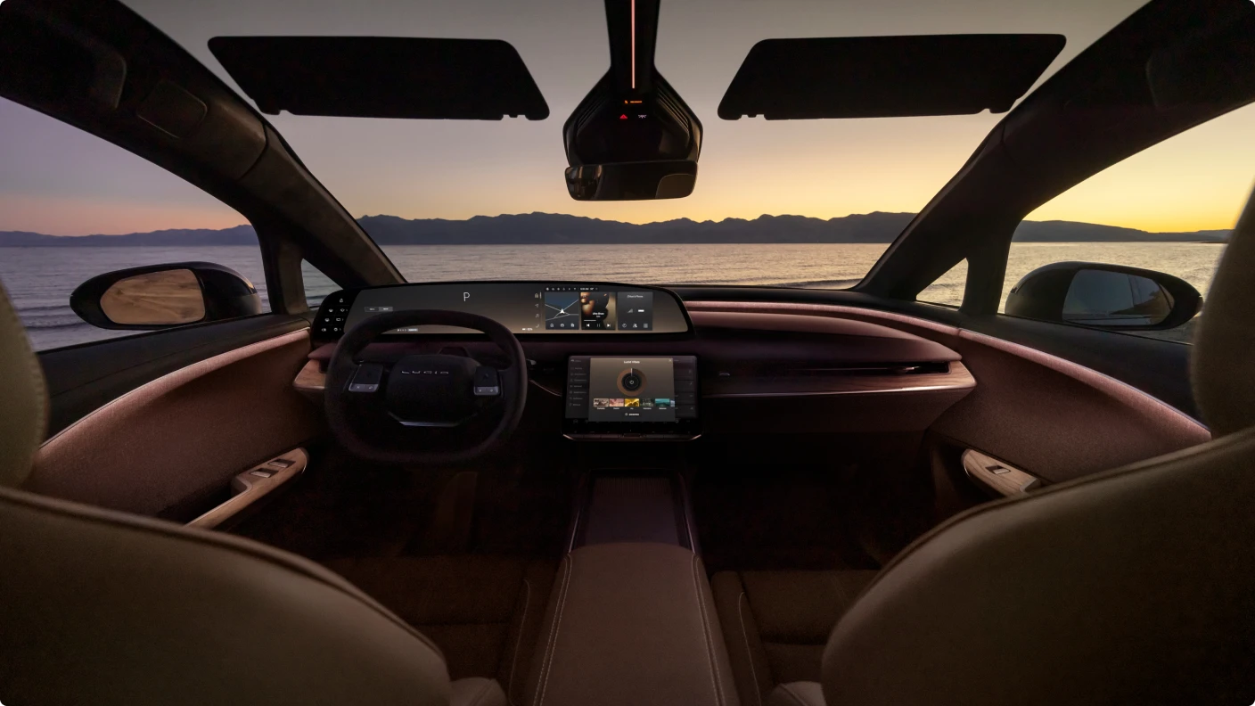 View from inside a luxury car with brown leather interior, digital dashboard, overlooking a lake at sunset with mountains.