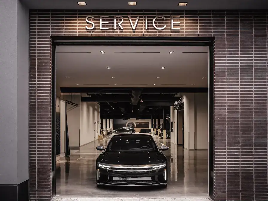 A sleek black luxury electric sedan parked inside a modern service center entrance with a lit "SERVICE" sign above.