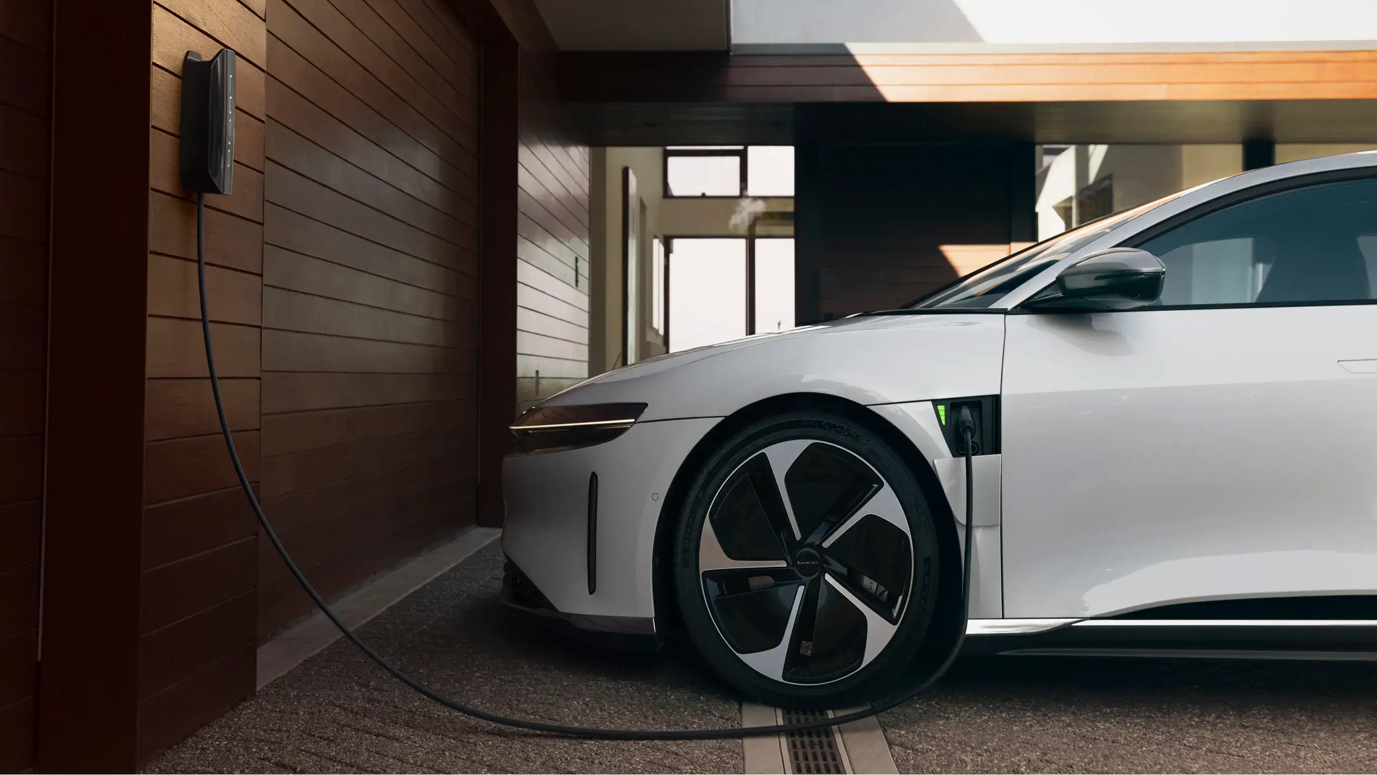 White electric car charging in a modern garage with wooden wall panels and a wall-mounted charging station.