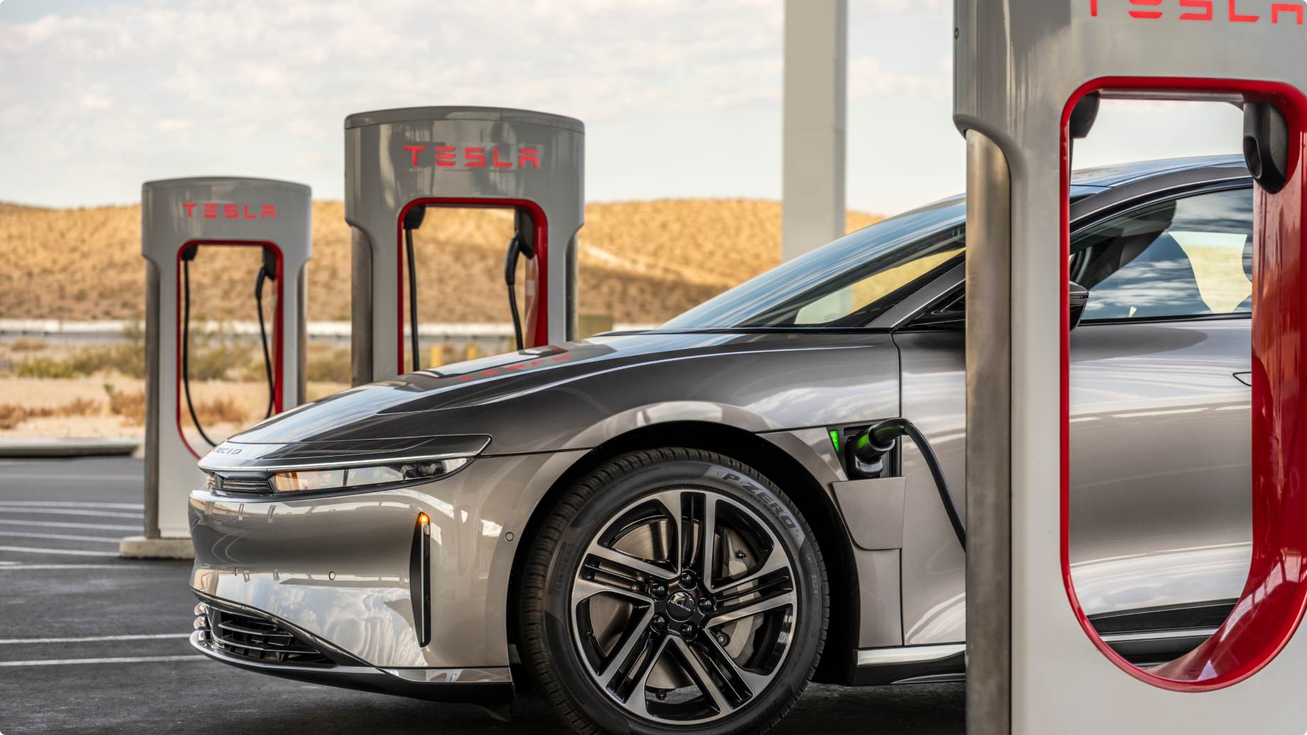 Lucid Air vehicle charging at Tesla Supercharger station with multiple charging units in desert landscape.