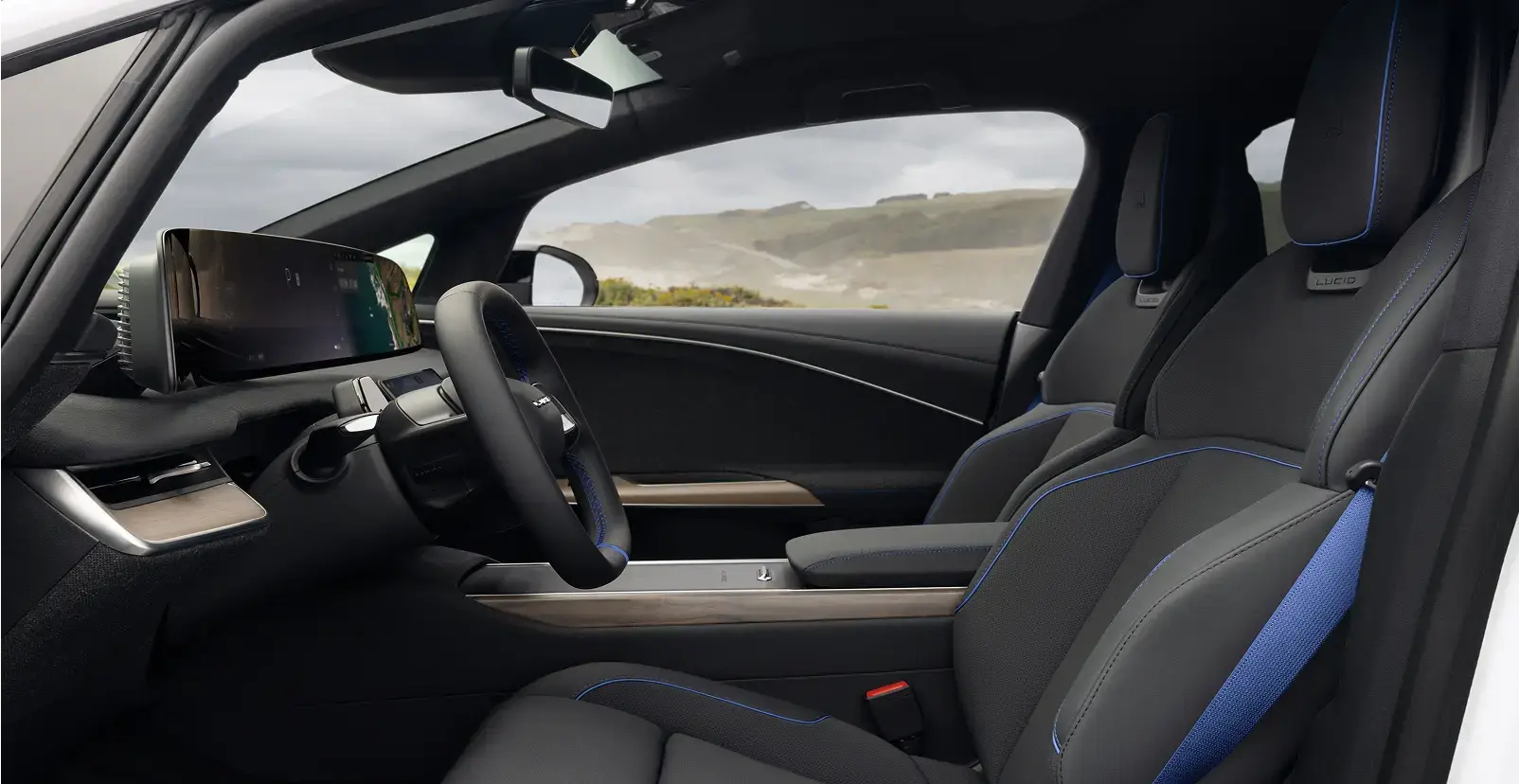 Lucid Air interior with dark seats featuring blue accents, a yoke-style steering wheel, large touchscreen, and wood trim console.