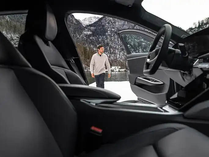 Vue à partir de l’intérieur d’une Lucid Air montrant une personne qui s’approche, avec des montagnes enneigées et un lac en arrière-plan.