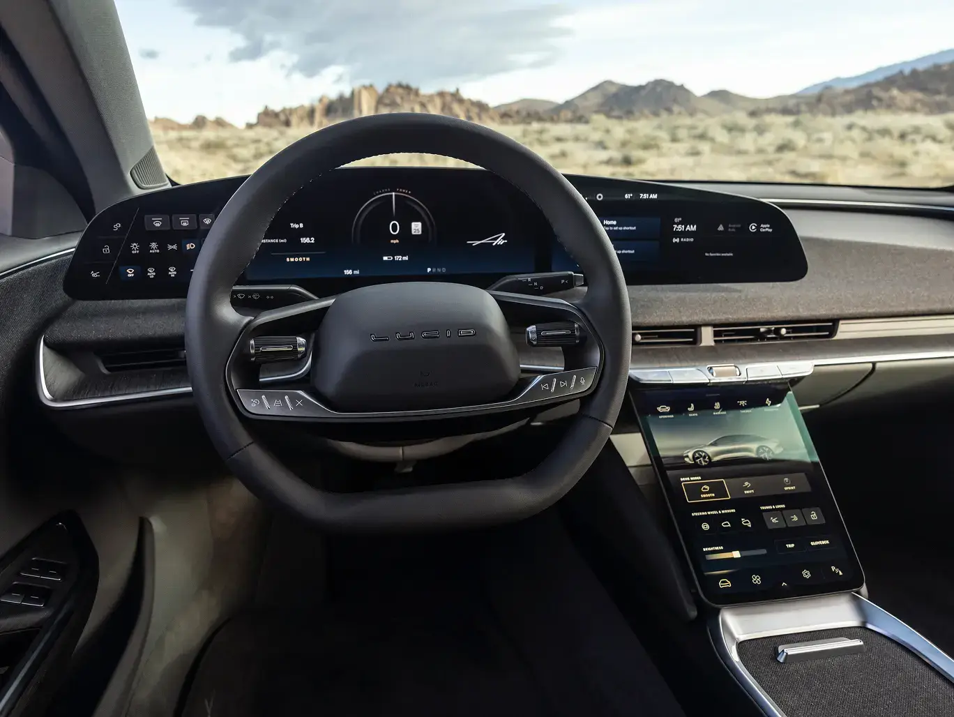 Modern car dashboard with digital displays and touchscreen interface, overlooking a desert landscape with mountains.