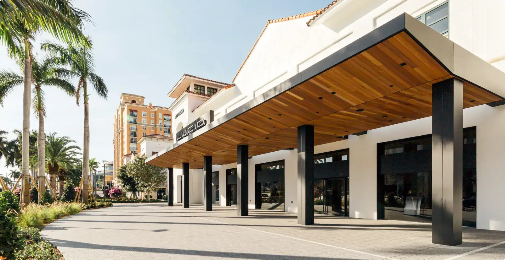 Lucid Motors showroom exterior with a wood-paneled canopy, black columns, palm trees, and a sunny Florida streetscape.