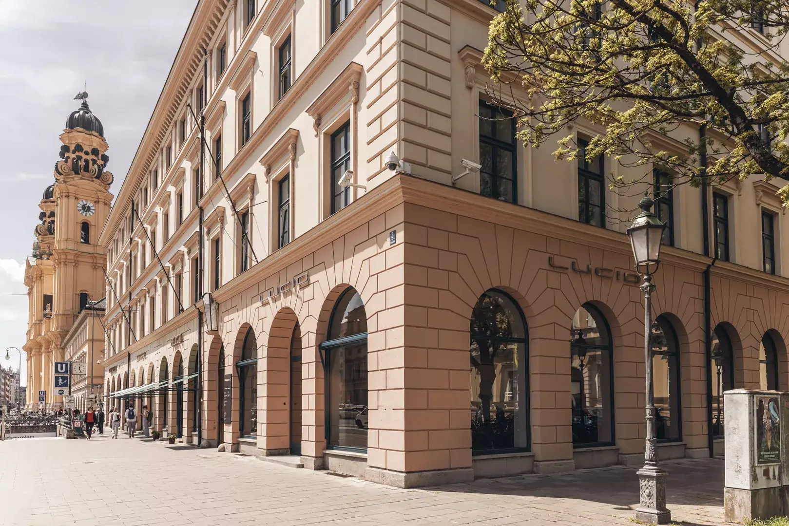 Die Aufnahme zeigt ein Lucid-Studio im historischen Süddeutschland. Es scheint die Sonne und die Farben sind warm. Es ist ein Baum, eine Straßenlaterne und ein altes Gebäude im Hintergrund zu sehen. 