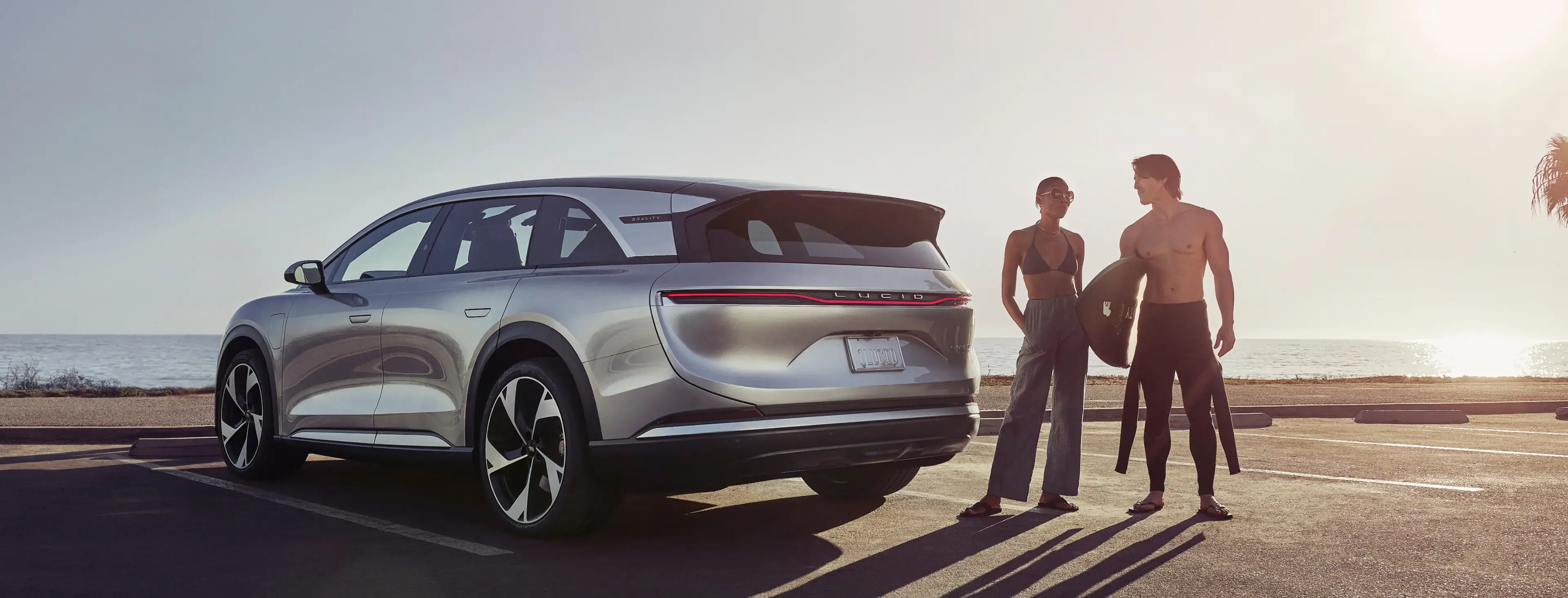 Lucid Gravity parked in beach parking lot with couple standing next to Lucid Gravity.